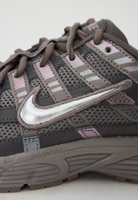 Baskets de sport grises avec une tige en mesh, un logo Nike en argent, des accents réfléchissants et une semelle texturée avec la marque "RIDELINER".