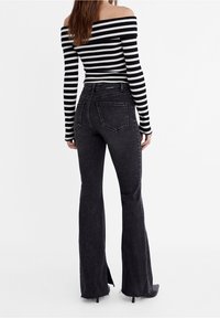 Zwarte flared jeans met een hoge taille, een versleten zoom en twee achterzakken, gecombineerd met een zwart-wit gestreepte off-shoulder top.