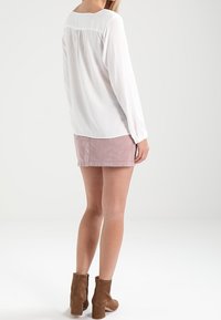 Blouse blanche à manches longues avec un détail froncé à l'arrière, associée à une mini-jupe en velours côtelé rose et des bottines brunes. Design simple et texturé.