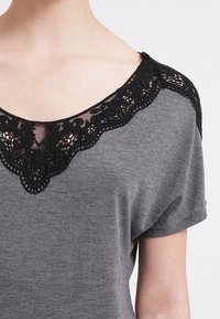 Szary top z krótkim rękawem z kwiatowym czarnym koronkowym dekoltem, miękką teksturą i luźnym krojem. Projekt zawiera szeroki dekolt w kształcie łódki.