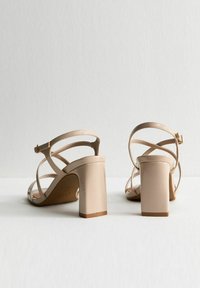 Nude-kleurige hoge hakken sandalen met een blokhak, voorzien van kruislingse bandjes en een enkelgesp, vervaardigd uit soepel synthetisch materiaal.