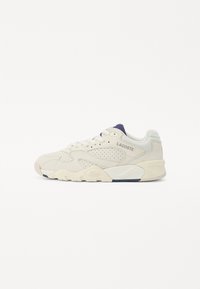 Lacoste-Sneaker in hellbeige mit durchbrochenem Design, runder Zehenpartie, flacher Schnürung und strukturiertem Profil. Beinhaltet ein marineblaues Akzentdetail.