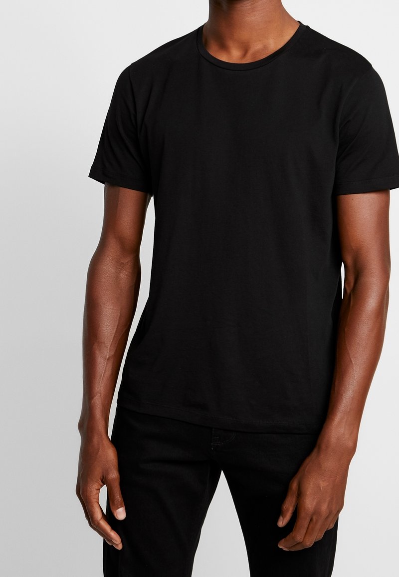 T-shirt en coton noir avec un col rond et des manches courtes, doté d'un design uni et d'une coupe régulière. Tissu texturé et accents minimaux.