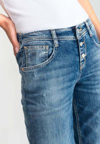Lichtblauwe denim jeans met een vijfknopen sluiting, versleten details en een enkele frontzak. Strak design met een lichte rek.