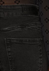 Jeans de mezclilla negra con un acabado texturizado, bolsillo trasero estándar y una etiqueta con "ONLY" en la cinturilla.