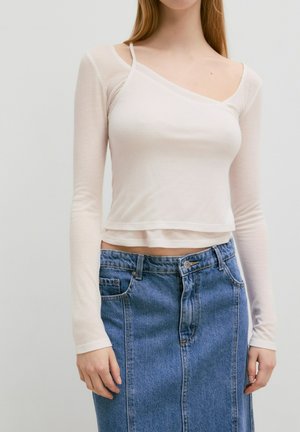 Lichtbeige langemouwige geribbelde top met een asymmetrische halslijn, gecombineerd met een denimrok die tot de knie reikt en een vooruitsparing en zakken heeft.