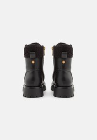 Bottines en cuir noir avec un col en fourrure noire moelleuse, des zips sur les côtés et une semelle en caoutchouc crantée. Quincaillerie en or à l'arrière.