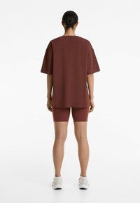 Bordeaux oversized t-shirt en bijpassende shorts tot boven de dij. Glad materiaal met een minimale uitstraling, gedragen met witte sportschoenen.