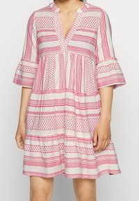 Robe à manches courtes en tissu léger avec des rayures rouges verticales et des motifs géométriques, dotée d'un col en V et d'une jupe à volants.