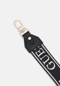 Sangle en tissu noir et blanc avec le texte "GUESS", attachée à un cuir noir et un crochet pivotant en métal argenté.