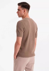 Suéter de punto beige de manga corta con un patrón texturizado, cuello redondo y corte ajustado, combinado con pantalones de color claro.