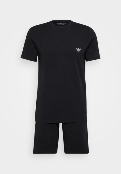 T-shirt nera in cotone a maniche corte abbinata a pantaloni corti neri. Presenta un piccolo logo bianco sul petto sinistro. Design semplice, vestibilità rilassata.