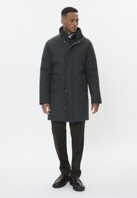 Tumšs, izolēts mētelis ar augstu apkakli, pogām un rāvējslēdzēja aizdari, kā arī divām priekšējām kabatām. Uzvilkts virs tumšām biksēm un apaviem.