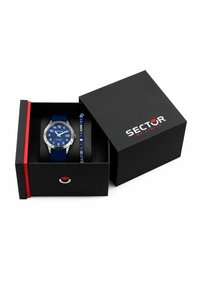 Orologio con cinturino in silicone blu, quadrante blu e bezel argentato, affiancato a un braccialetto di perline, all'interno di una scatola nera con accenti rossi e blu.
