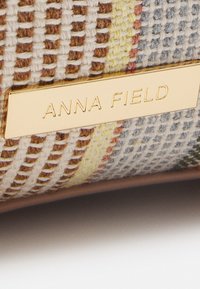 Torebka pleciona z teksturowanej, wielobarwnej tkaniny z metalową plakietką z wygrawerowanym napisem "ANNA FIELD" na gładkiej podstawie.