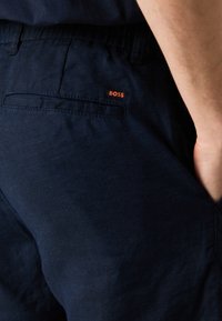 Shorts in lino blu navy con una tasca posteriore decorata da un'etichetta rossa con logo "BOSS" e una superficie di tessuto liscia e testurizzata.