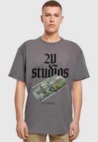 Šedé bavlněné tričko s volným střihem, na kterém je výrazný černý text a grafika dvacetidolarové bankovky s designem žiletky.