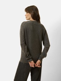 Maglione grigio scuro realizzato in material morbido, con scollatura rotonda e polsini a costine, abbinato a jeans scuri, visto da dietro.