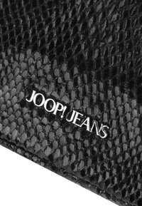 Črn denarnica z teksturo, opremljena z vzorcem reptila, s sijočim srebrnim logotipom "JOOP! JEANS", ki je na prominentnem mestu.