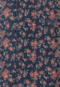 Navy bloemenpatroon stof met kleine rode en witte bloemen, groene bladeren en een zigzaglogo, met een gladde textuur.