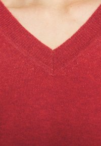 Närbild av en persons övre bröst som bär en röd V-ringad stickad tröja som visar hud ovanför halsringningen.