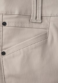 Beige látka z bavlněné směsi s diagonálním designem kapes, viditelným švem a černými kovovými akcenty na okrajích kapes.