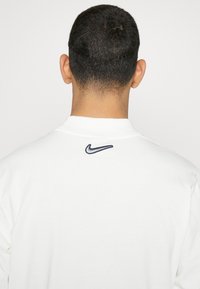 White Nike sweatshirt featuring a crew neckline and navy embroidered logo on the back. Textured fabric with long sleeves.
