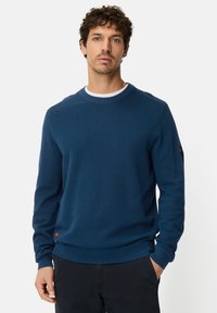 Navy crewneck sweater made of textured knit fabric, featuring ribbed cuffs and hem, with a small brand tag on the left sleeve.