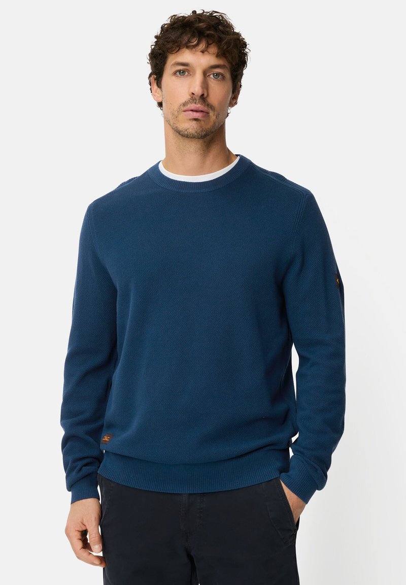Navy crewneck sweater made of textured knit fabric, featuring ribbed cuffs and hem, with a small brand tag on the left sleeve.