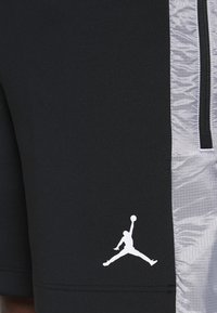 Svarta sportshorts i slät, elastisk tyg med en blank silverfärgad sidopanel och en vit Jumpman-logotyp nedanför till vänster.