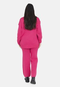 Rosa gestrickter Pullover und passendes Hosen-Set. Der Pullover hat überschnittene Schultern; die Hose hat einen lockeren Schnitt mit gerippten Bündchen. Strukturierte Strickoberfläche.