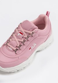 Pink Fila sneakers with a smooth synthetic upper, silver hardware, and a textured white outsole. Features a looped back pull tab and lace-up design.
