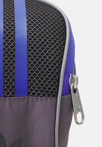Purple and black zippered pouch made of textured fabric, featuring mesh detailing, two purple stripes, and a silver zipper pull with logo.