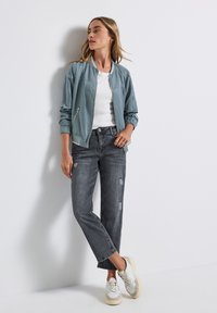 Veste bomber bleu clair avec des poignets élastiques, t-shirt blanc, jean gris déchiré et baskets crème. Design minimaliste avec une coupe décontractée.