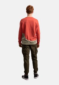 Rode en grijze sweatshirt met een relaxte pasvorm, contrasterend onderpaneel en geribde manchetten, gecombineerd met donkergroene cargo-broeken en zwarte sneakers.