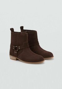 Par de botas de ante marrón oscuro hasta el tobillo con tacones de madera bajos y cremallera lateral, que presentan correas decorativas y remaches metálicos.