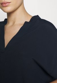 Primo piano di una persona che indossa una blusa blu scuro con colletto a V e una texture di tessuto liscia.