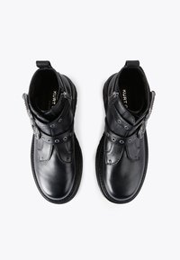 Czarne skórzane botki za kostkę ze srebrnymi dodatkami, z okrągłym noskiem, detalami w postaci pasków oraz teksturowaną podeszwą. Uzupełnione o zamek błyskawiczny z boku.