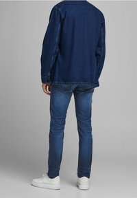 Mörkblå denimjacka med avslappnad passform, kombinerad med smala mörka jeans och vita sneakers. Enkel design utan synliga mönster eller detaljer.