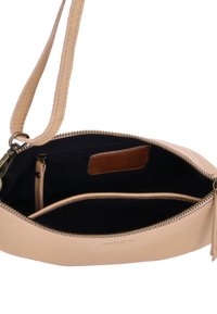 Beżowa skórzana torebka crossbody z zamkiem błyskawicznym, wewnętrznymi kieszeniami oraz ciemnonawowym wykończeniem. Charakteryzuje się gładką teksturą i brązowymi akcentami.