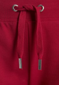 Red cotton blend sweatpants featuring a ribbed waistband with silver eyelets and a braided drawstring with metal tips.