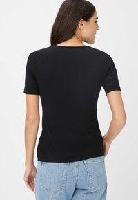Sort kortærmet t-shirt med rund halsudskæring og tætsiddende design. Stof er glat og strækbart, parret med lyseblå denim jeans.