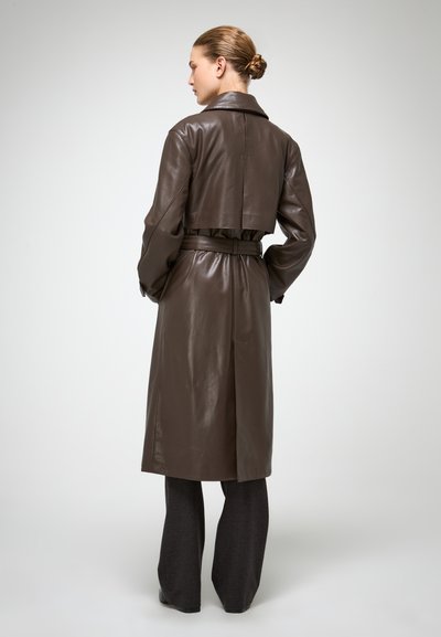 Bruine leren trenchcoat met een ceintuur in de taille, gekerfde kraag en een kortere achterkant. De stof heeft een gladde, glanzende textuur.