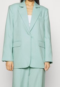 Blazer oversize verde menta chiaro realizzato in tessuto testurizzato, con due tasche frontali e colletto a punta. Design sartoriale con maniche larghe.