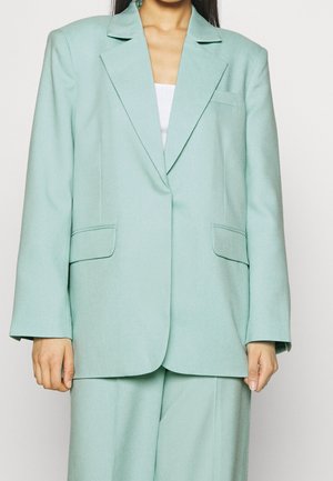 Blazer oversize verde menta chiaro realizzato in tessuto testurizzato, con due tasche frontali e colletto a punta. Design sartoriale con maniche larghe.