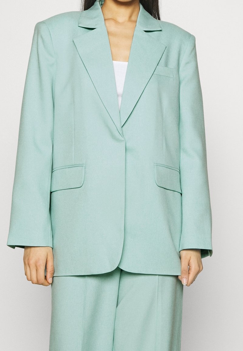 Blazer oversize verde menta chiaro realizzato in tessuto testurizzato, con due tasche frontali e colletto a punta. Design sartoriale con maniche larghe.