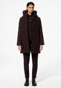 Giacca imbottita in prugna scuro con cappuccio, dotata di zip frontale, bottoni a scatto e texture trapuntata, abbinata a pantaloni fitted coordinati e stivaletti neri.