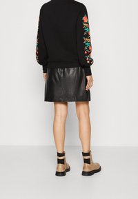 Černá mikina s květinovou výšivkou na rukávech, doplněná o černou koženou sukni a béžové kotníkové boty s černými detaily.