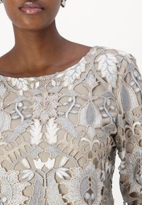 Besticktes Kleid mit beigem Grund, einer zarten Textur und intricaten silbernen sowie cremefarbenen Blumenmustern, Rundhalsausschnitt.