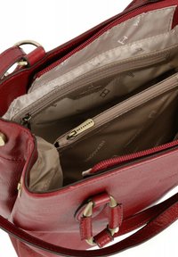 Borsa a tracolla rossa in pelle con hardware dorato. L'interno presenta una fodera beige, scomparti con zip e dettagli logati. Design strutturato.